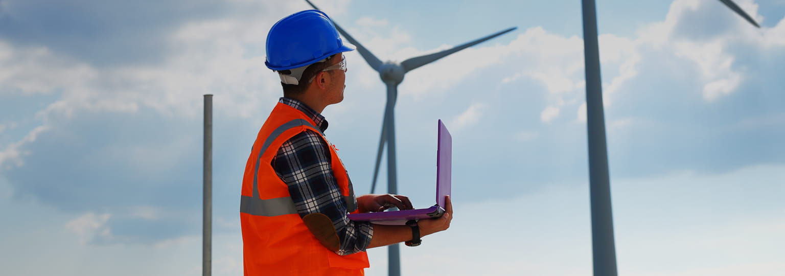 Man in hard hat with a laptop in a wind farm