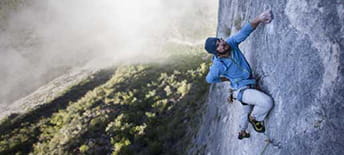 Man climbing side of mountain with one hand 